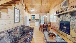 Ein Holzblockhaus-Interieur mit Holzbalkendecke, Kamin aus Stein, Essbereich und einer Couch.