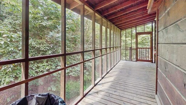 Eine überdachte Holzterrasse mit großen Fenstern, umgeben von Bäumen.