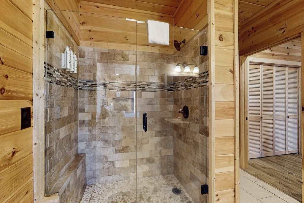 A wooden cabin interior with a glass-enclosed shower area, wooden walls, and a visible door with louvered shutters.
