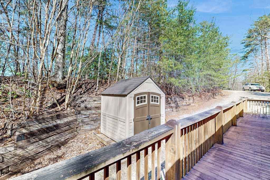 Une terrasse en bois mène à un petit abri doté d’une porte, le tout étant entouré d’arbres.