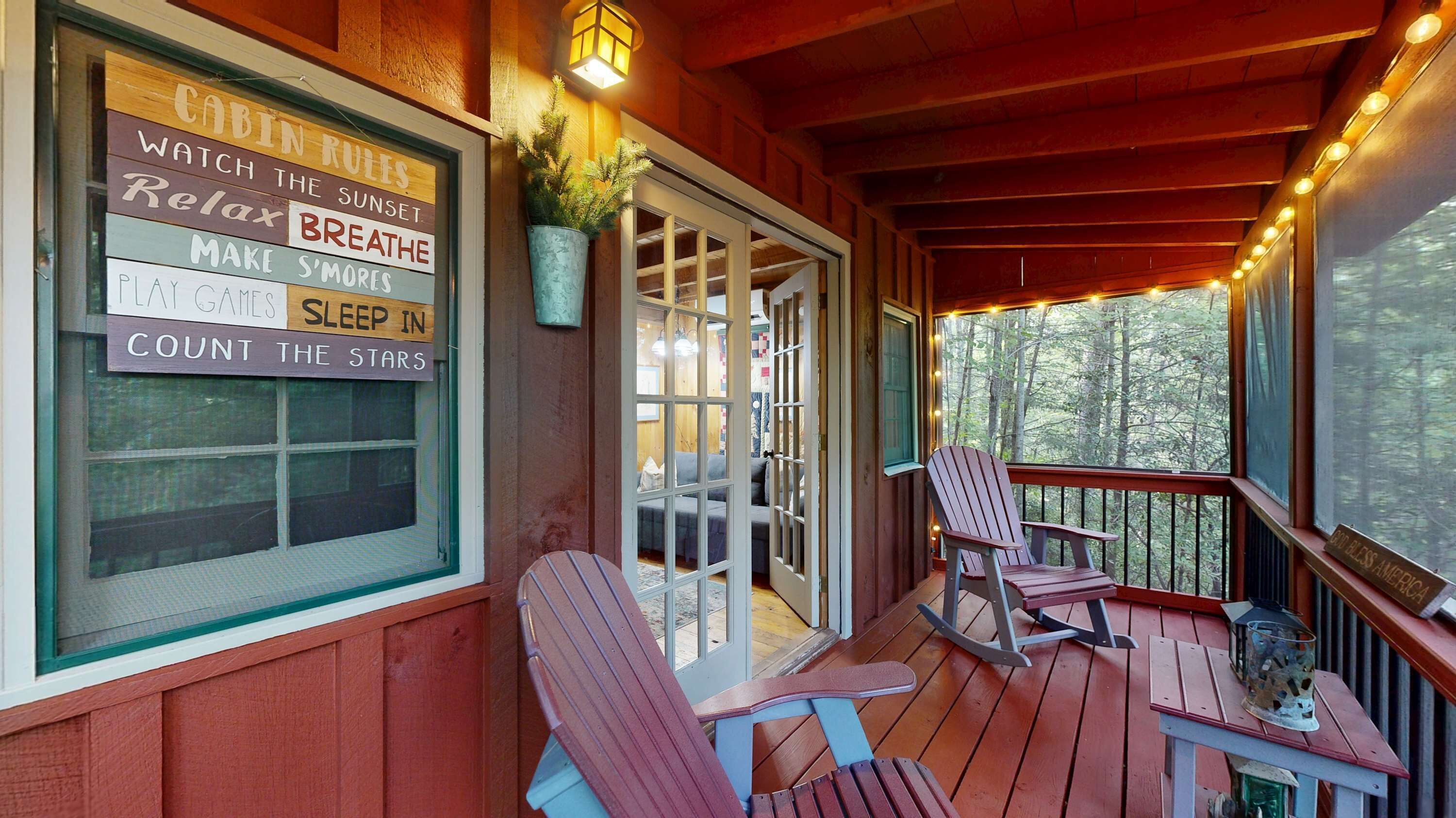 A wooden deck with Adirondack chairs, a rocking chair, and a table with a lantern. A sign with cabin rules is visible on the wall.