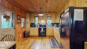 Cocina de cabaña de madera con refrigerador, estufa, microondas y gabinetes de madera.