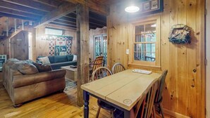 Interior de una cabaña de madera con una mesa de comedor, sillas, un sofá y una escalera.