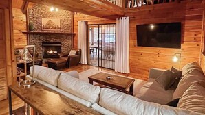 Ein gemütliches Blockhaus-Interieur mit Kamin aus Stein, Holzwänden, einer Couch und einem an der Wand befestigten Fernseher.