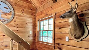 Ein Holzblockbau-Innenraum mit einem aufgehängten Hirschgeweih, einem Fenster und einer Holztreppe.