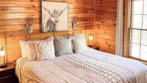 Ein schlicht eingerichtetes Schlafzimmer im Chalet-Stil mit einem Bett, Kissen, einem gerahmten Bild und Wandleuchten.