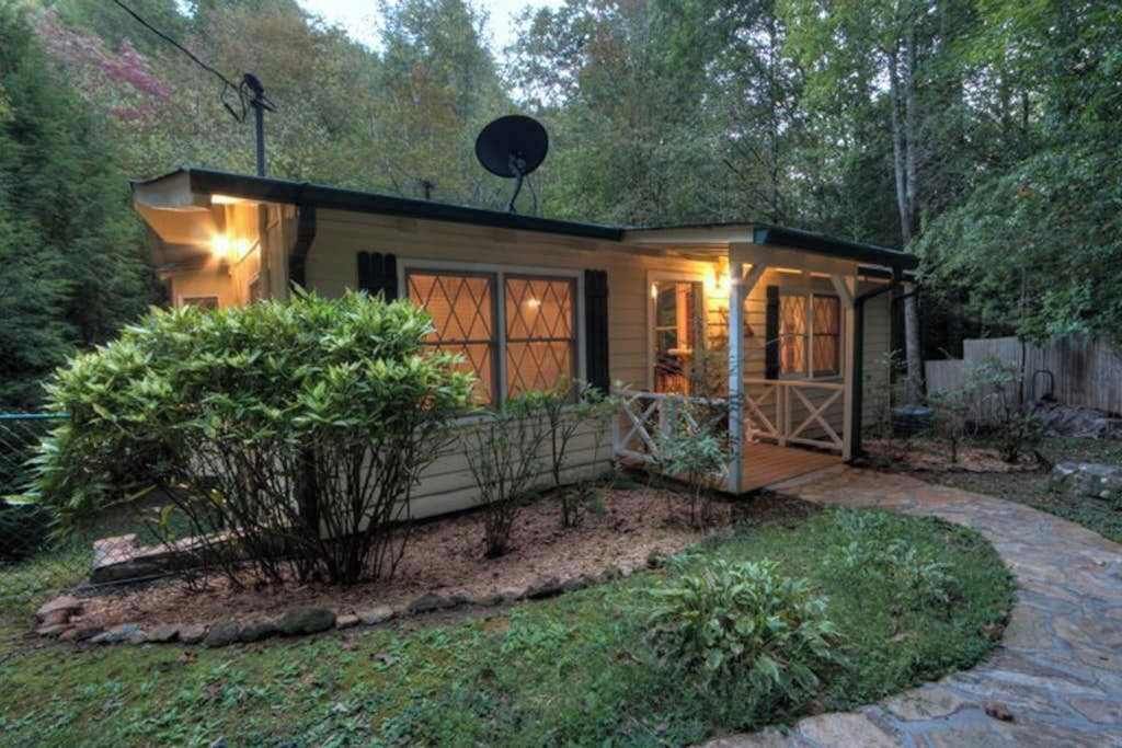 A small, single-story house with a covered porch, a satellite dish, and a stone pathway leading to the entrance.