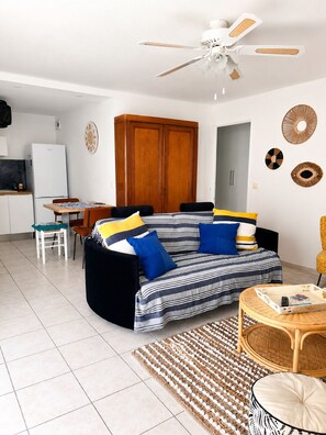 A living room with a sofa, a dining table, a kitchen area, and a ceiling fan. - BETWEEN THE HARBOR AND THE BEACH (Marseillan)