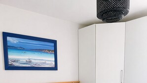 A bedroom with a bed, pillows, a bedside table, a lamp, a framed picture, a wardrobe, and a rug. - BETWEEN THE HARBOR AND THE BEACH (Marseillan)