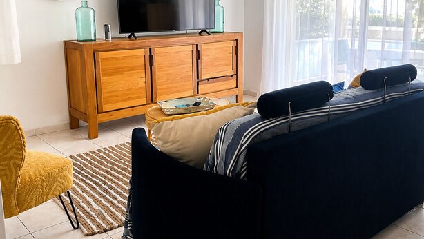 A modern living room with a sofa, a wooden cabinet, a television, and a ceiling fan. - BETWEEN THE HARBOR AND THE BEACH (Marseillan)