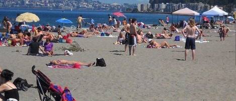 A beach with people sunbathing, umbrellas, and a stroller.