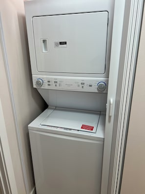 Eine kompakte, weiße Waschmaschine mit Bedienfeld, einem QR-Code und einem roten Sicherheitshinweis.