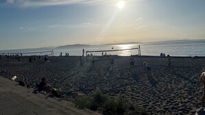 En volleyballbane ved stranden med spillere, et net og en klar himmel.
