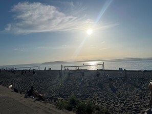 Ein Beachvolleyballfeld mit Spielern, einem Netz und blauem Himmel.