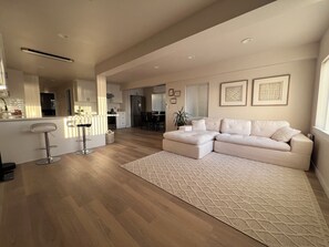 Una sala de estar moderna con sofá, zona de comedor y cocina al fondo.