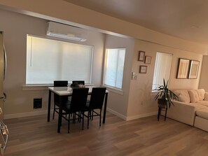 Ein modernes Wohnzimmer mit Essbereich, ausgestattet mit einem großen Fenster, einem Sofa und einer Kübelpflanze.