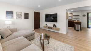 A living room with a sofa, TV, and a kitchen area visible through an open door. - Quiet retreat, spacious living and dining (Sioux Falls)