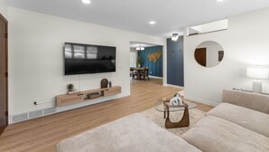 A modern living room with a flat-screen TV, a sofa, a coffee table, and a dining area in the background. - Quiet retreat, spacious living and dining (Sioux Falls)