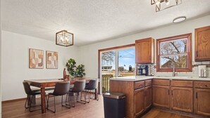 Een moderne keuken met houten kastjes, een eethoek met een tafel en stoelen, en een groot raam met uitzicht op de omgeving.