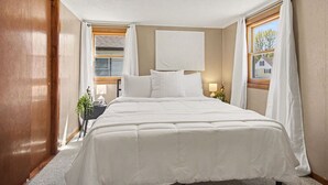 Een slaapkamer met een groot bed, een nachtkastje, een lamp en een raam met gordijnen.