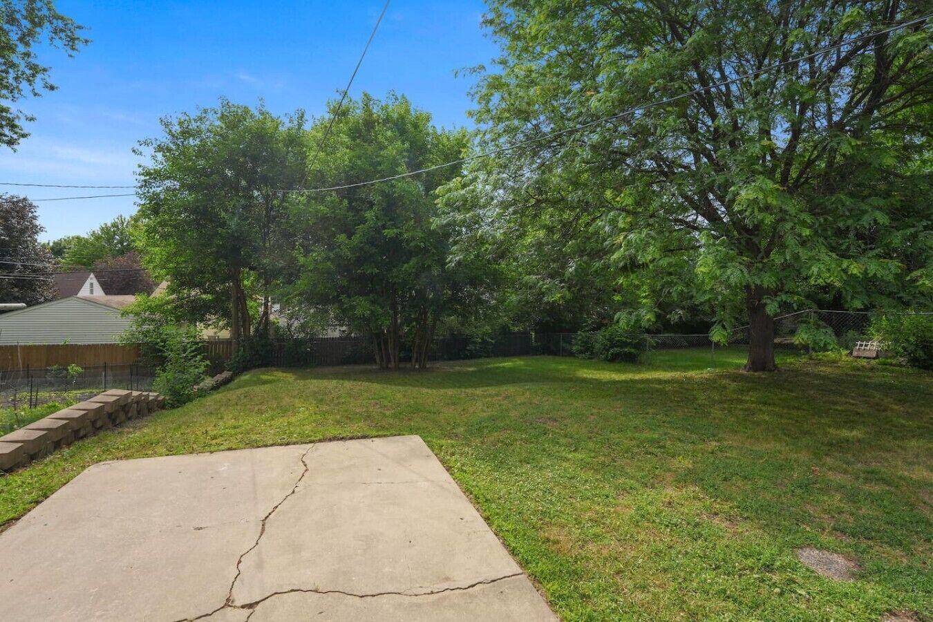 Un patio trasero con un sendero de hormigón, árboles y una valla.