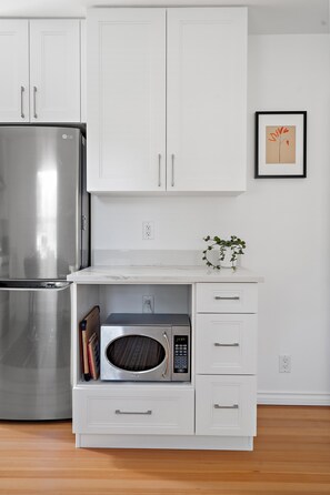 A kitchen with a stainless steel refrigerator, a microwave, and white cabinetry. - Charming Seaside Cottage in Victoria's Historic Core (Victoria South)