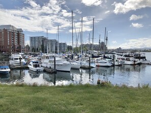 A marina with multiple boats docked, a grassy foreground, and buildings in the background. - Charming Seaside Cottage in Victoria's Historic Core (Victoria South)
