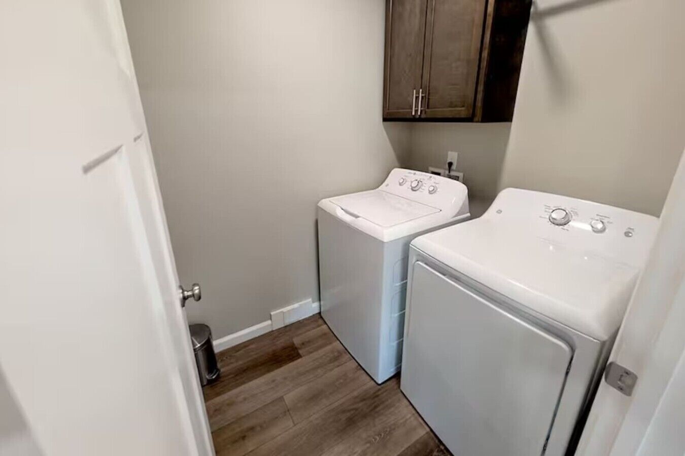 A laundry room with two white washers and dryers, wooden flooring, and a cabinet above the dryers.
