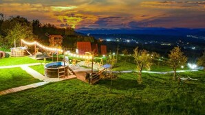 Un espacio al aire libre con piscina, construcciones de madera y vista a una ciudad distante al atardecer.