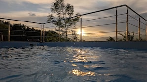 Una piscina con vista al atardecer, rodeada por una cerca metálica y árboles.