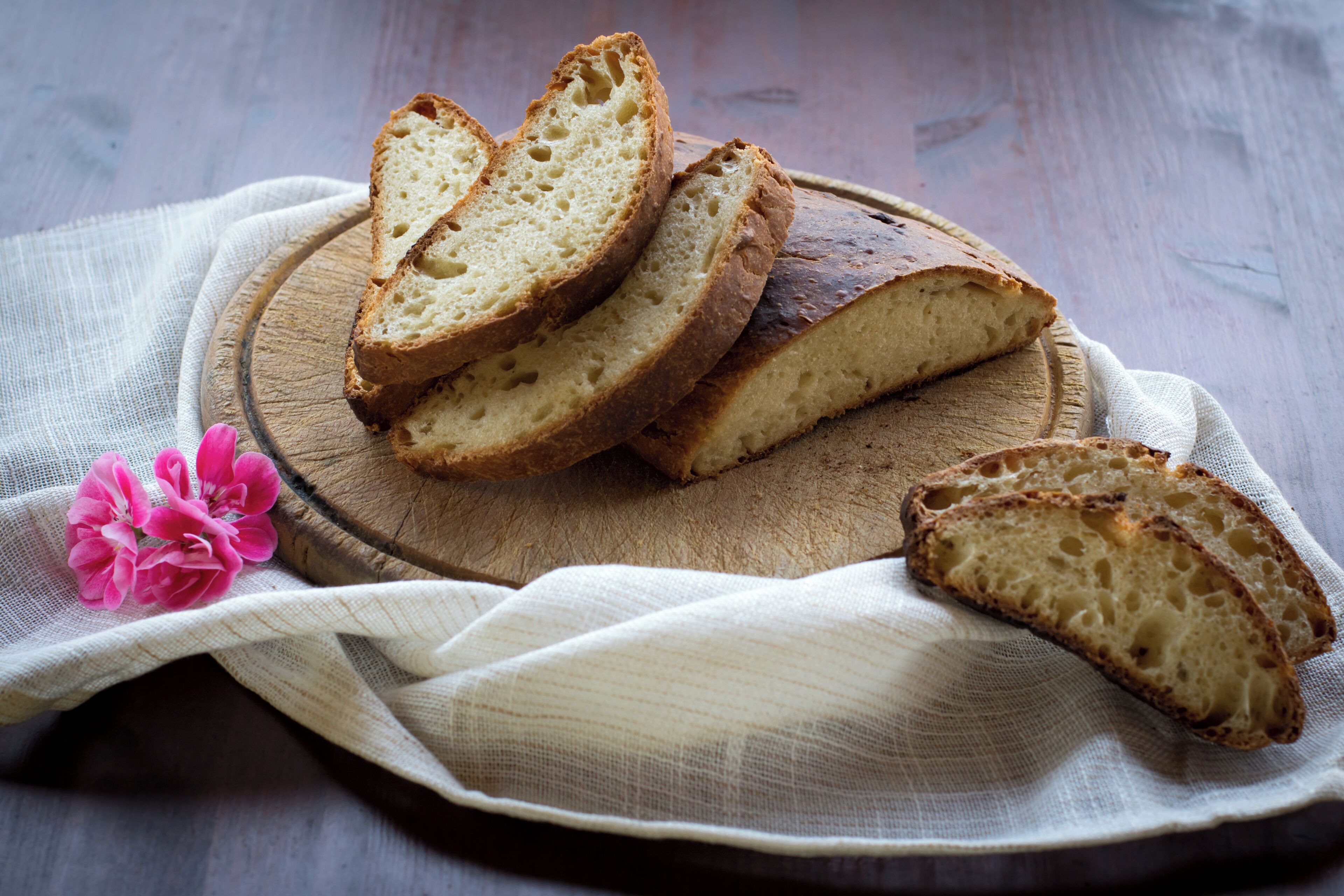 Fette di pane su un tagliere di legno con un panno e fiori rosa.