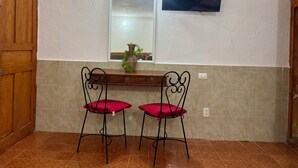 Una habitación con puerta de madera, piso de baldosas, televisor de pantalla plana en la pared y dos sillas rojas con cojines.