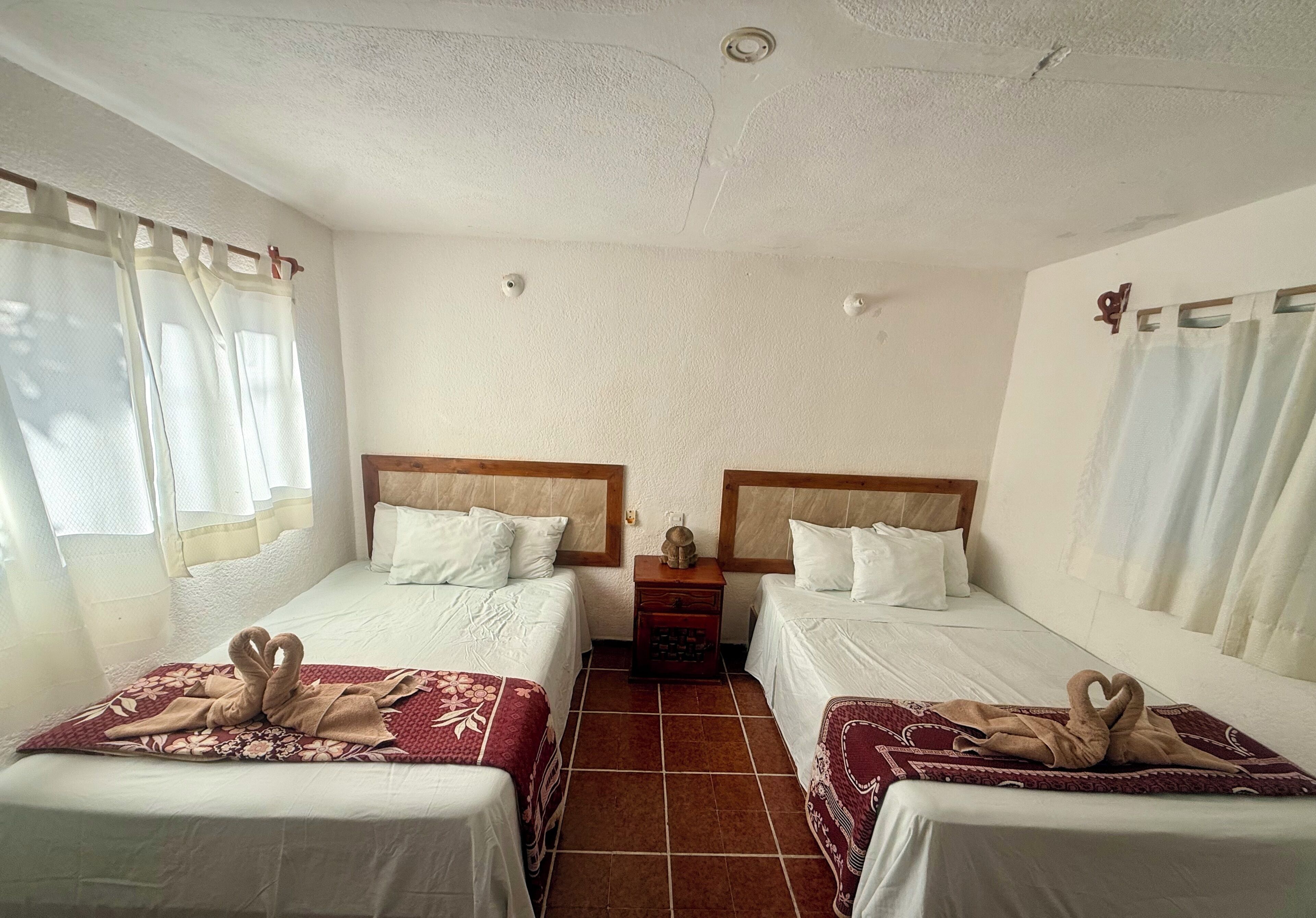 A hotel room with two beds, a nightstand, and a window with curtains.