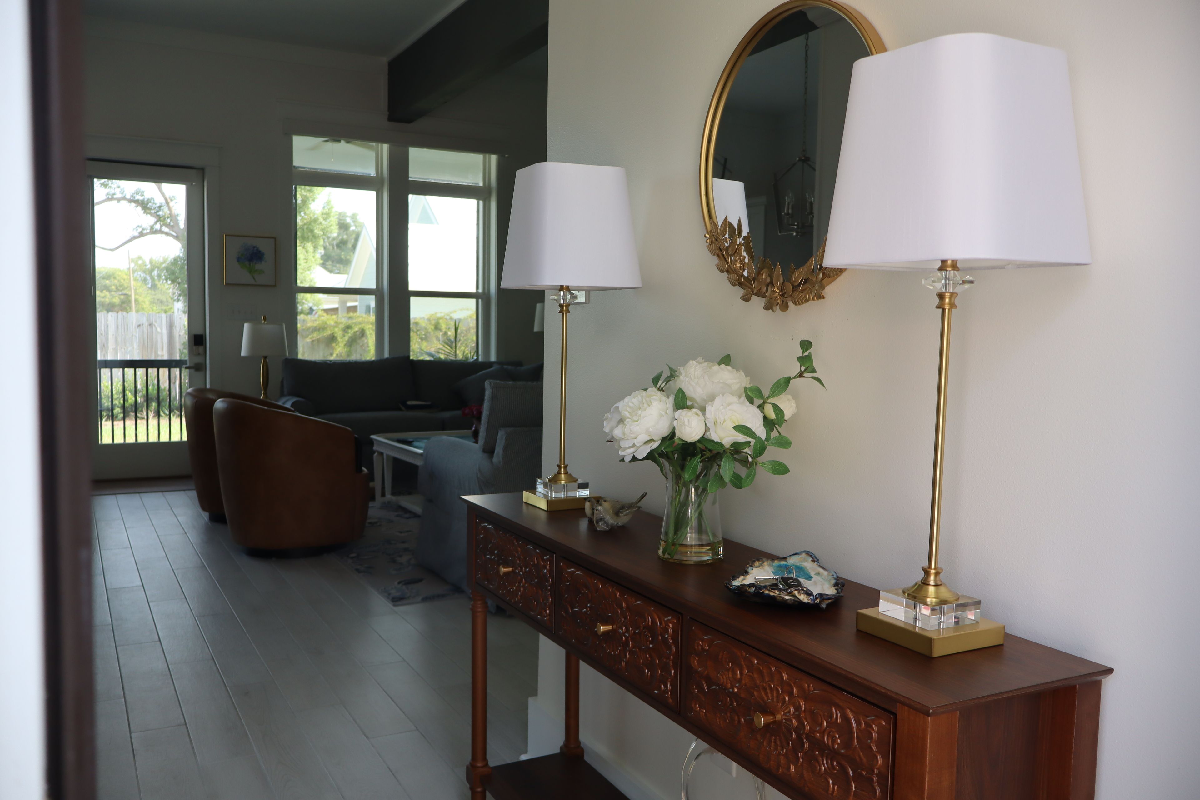 A living room with a wooden console table, two lamps, a vase with flowers, and a large mirror on the wall.