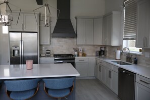 A modern kitchen with stainless steel appliances, a central island with bar stools, and a large window with blinds. - Perfect for your Baycation! Comes with 4 person golf cart. (Bay St. Louis)
