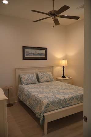 A bedroom with a bed, a nightstand, a lamp, a ceiling fan, and a framed picture on the wall. - Perfect for your Baycation! Comes with 4 person golf cart. (Bay St. Louis)