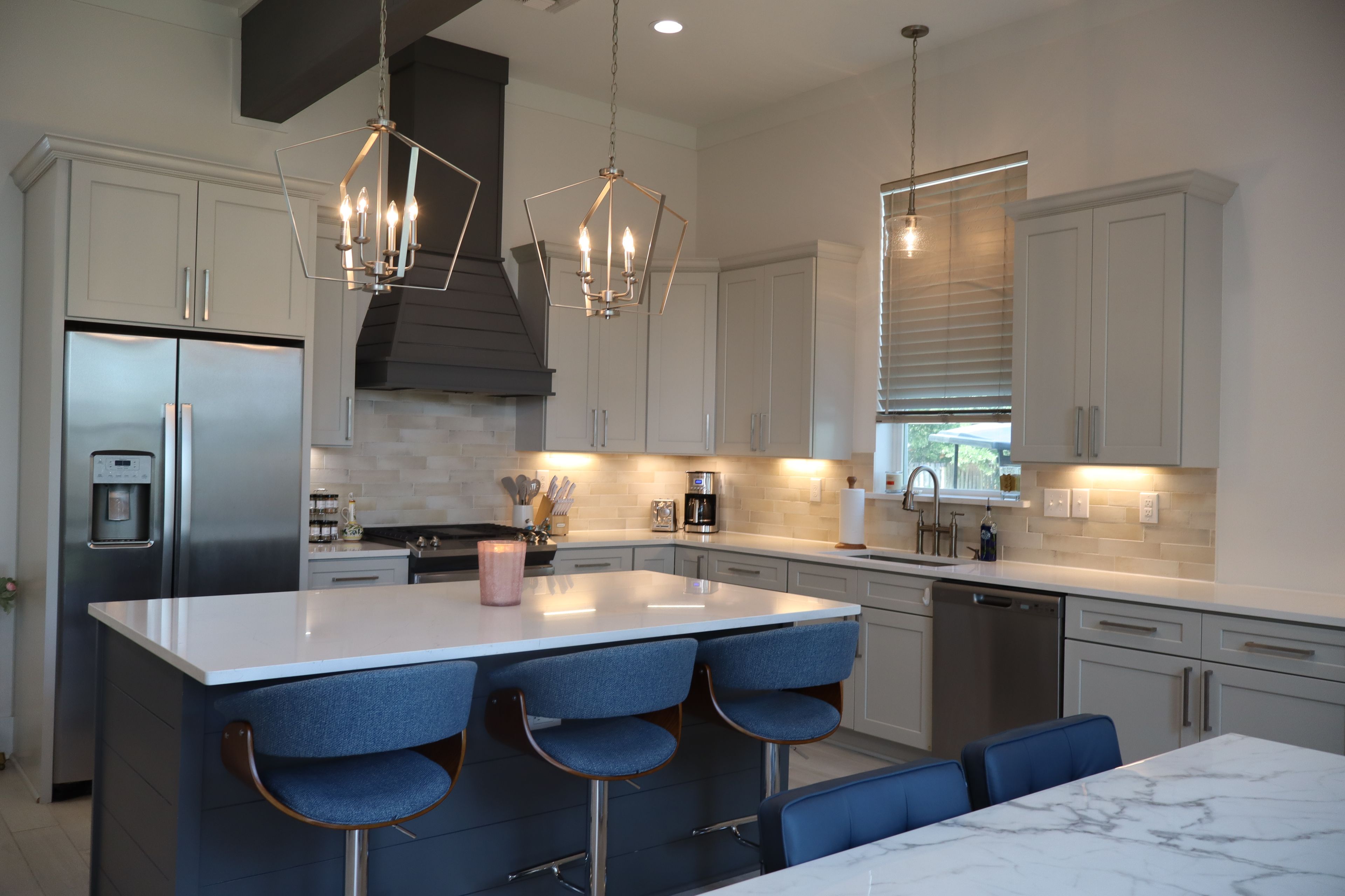 A modern kitchen with a central island, bar stools, stainless steel appliances, and pendant lighting.