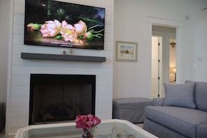 A living room with a flat-screen TV mounted above a fireplace, a sofa, and a small table with a vase of flowers. - Perfect for your Baycation! Comes with 4 person golf cart. (Bay St. Louis)