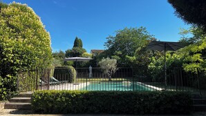 En pool med staket runt om och trappsteg som leder ner i vattnet, omgiven av grönska och en klar, blå himmel.