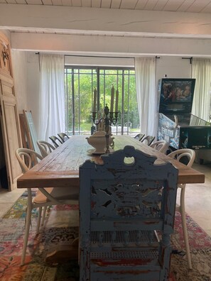 Un espace repas avec une table en bois, des chaises blanches, un tapis à motifs et une vue dégagée grâce à de grandes fenêtres.