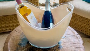 Udsigt til stranden med en fletstol, en polstret sofa og en glas isspand med to flasker vin.