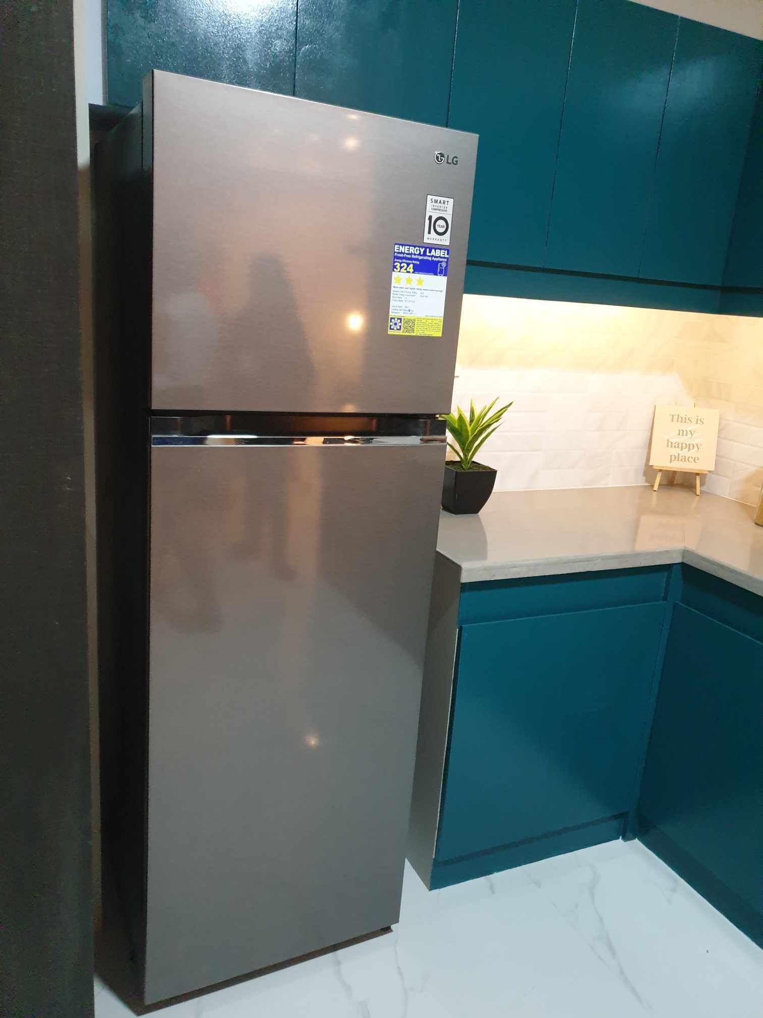 A stainless steel LG refrigerator in a kitchen with teal cabinetry and a white countertop.