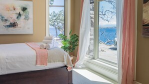 Une chambre à coucher avec un lit, une fenêtre donnant sur la mer et un tableau accroché au mur.