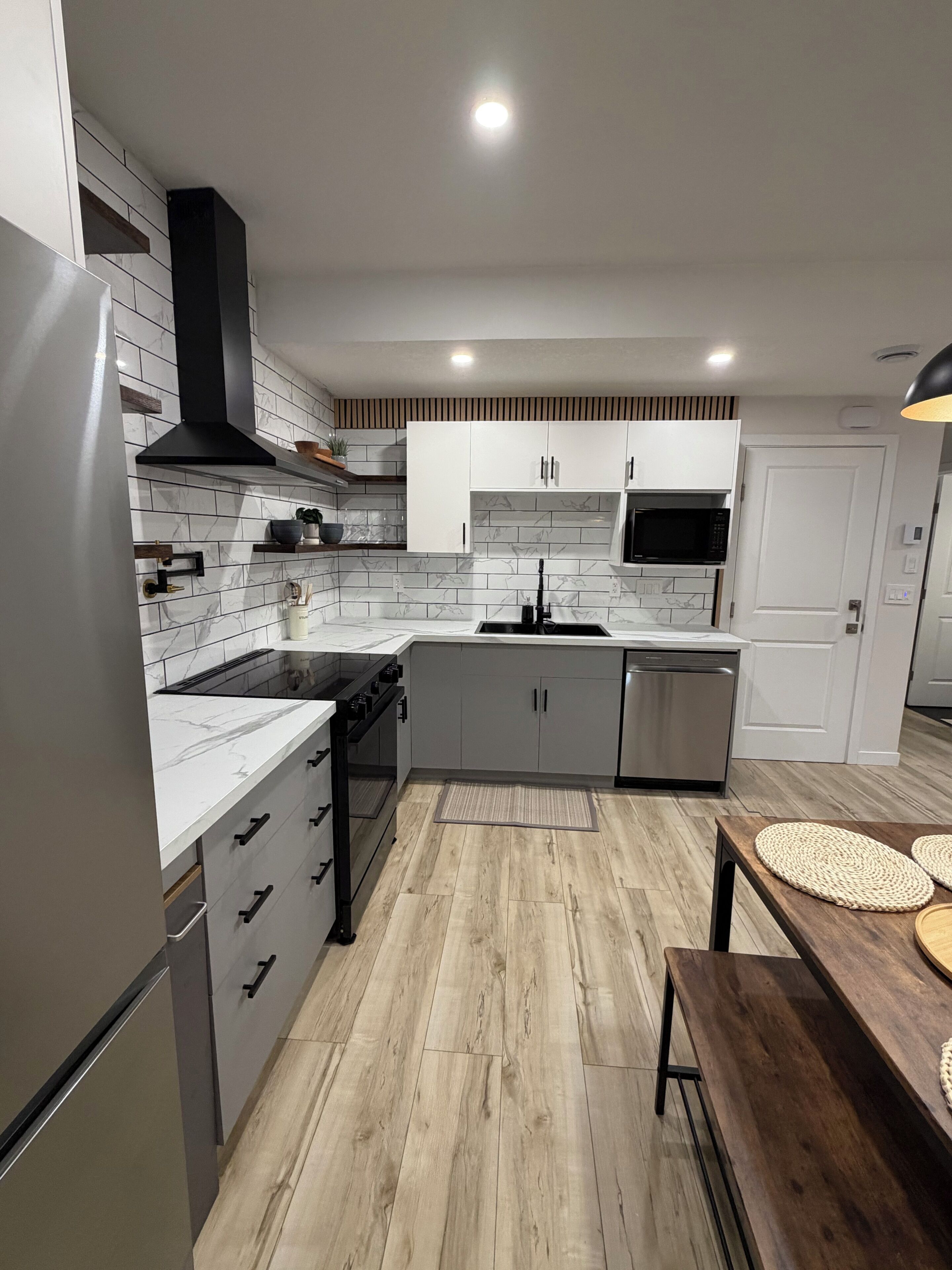 A modern kitchen with white cabinets, a stainless steel refrigerator, a microwave, and a wooden dining table.