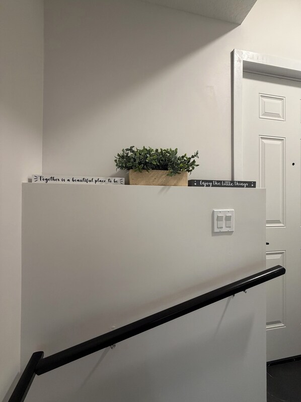 A white wall with a potted plant, a sign with a quote, and a door.