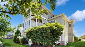 A two-story residential building with a balcony, a well-maintained lawn, and a large tree in the foreground. - Rehoboth Beach - 24 Brooklyn Ave Unit E (Rehoboth Beach)