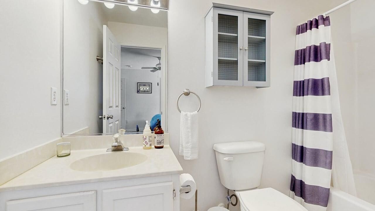A bathroom with a sink, mirror, cabinet, toilet, and striped shower curtain.