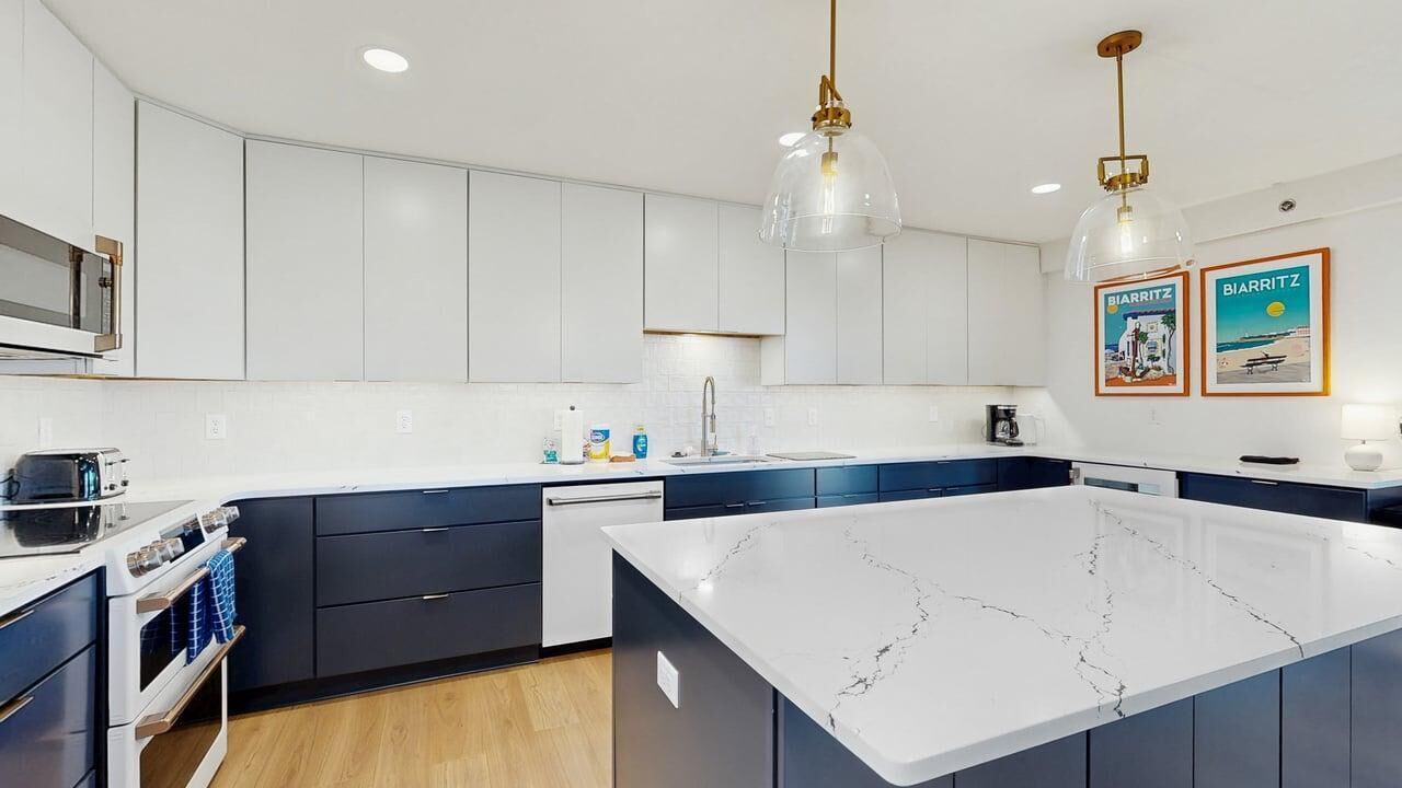 A modern kitchen with white cabinets, a marble island, and pendant lighting.