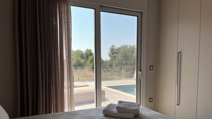 Een slaapkamer met een groot bed, uitzicht op een zwembad en een schuifdeur.