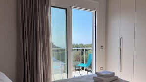 Een slaapkamer met een bed, een raam met gordijnen, een balkon met een stoel en uitzicht op groen.